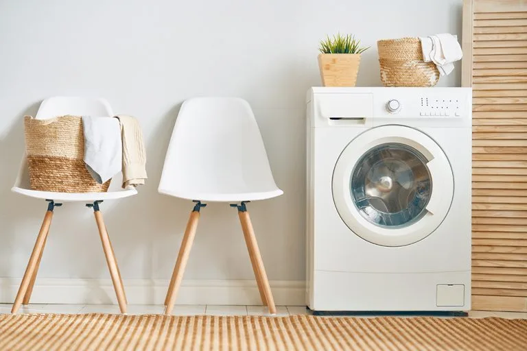 A front-loading washing machine beside chairs and laundry baskets.