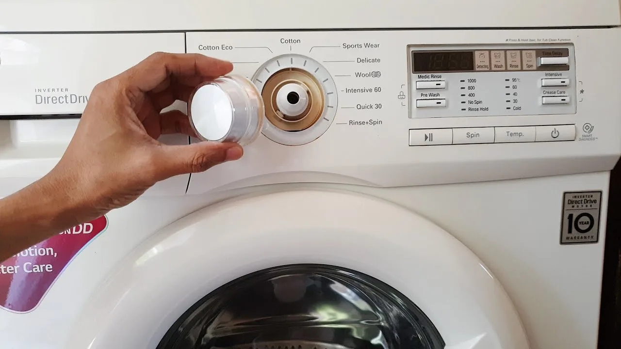 A hand holding a removed control knob in front of a washing machine control panel.