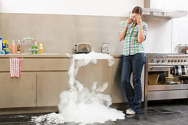 A person beside a dishwasher with suds spilling onto the kitchen floor.