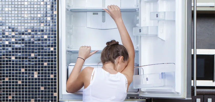 A person looking into an open, empty refrigerator.
