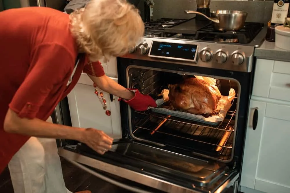 A person using oven mitts to move a roasting pan inside an oven.